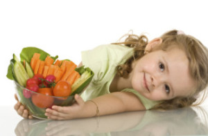 Little girl leaning on the table with a bowl of vegetables - isolated